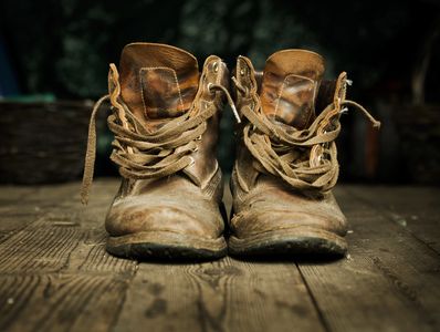 A pair of worn-out brown leather boots on a wooden floor.