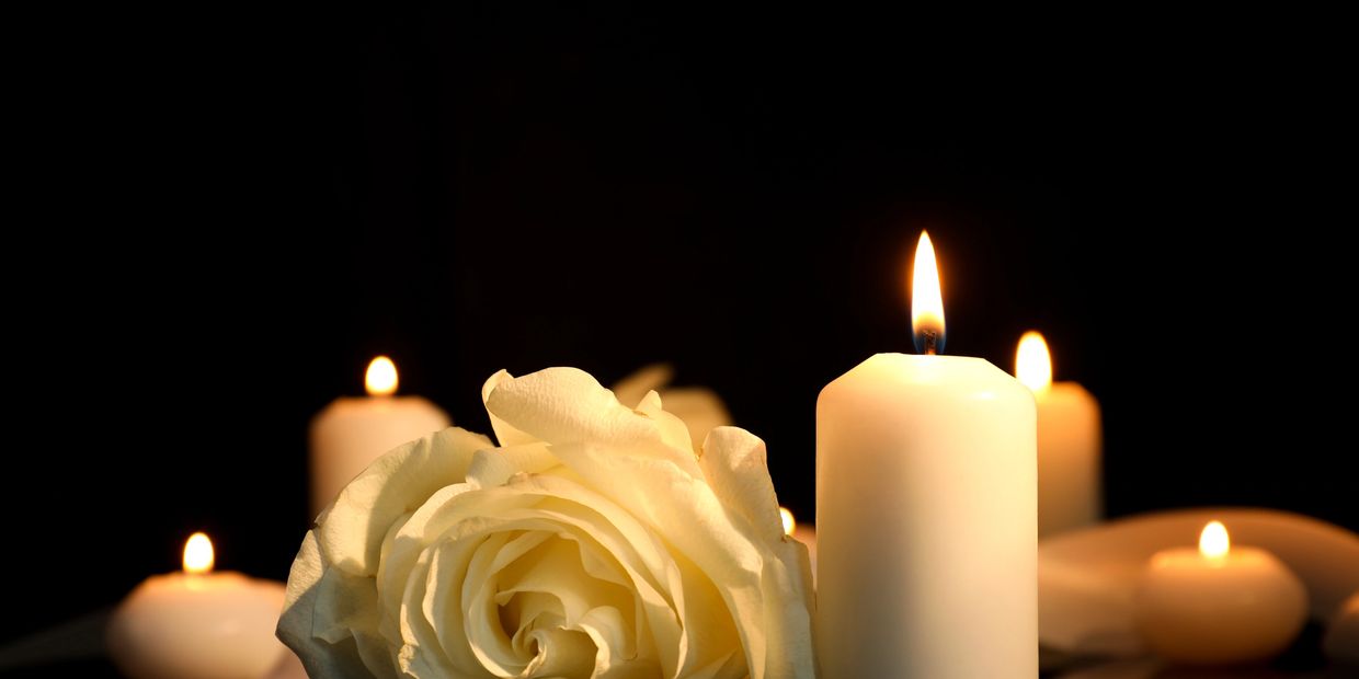White rose and lit candles in a dark setting.