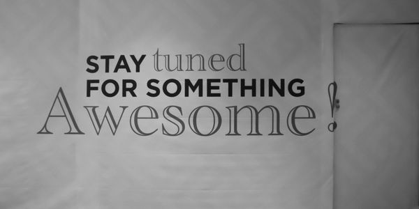 Motivational wall text reading 'Stay tuned for something awesome!' in black and red.