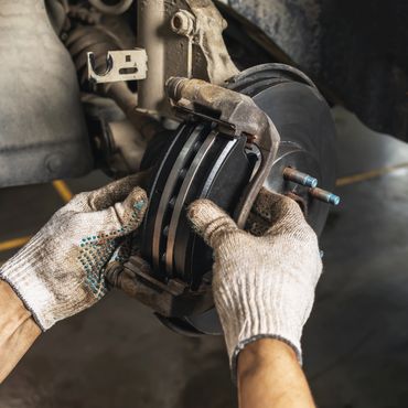 Gloved hands installing new brake pads on a car's disc brake system.