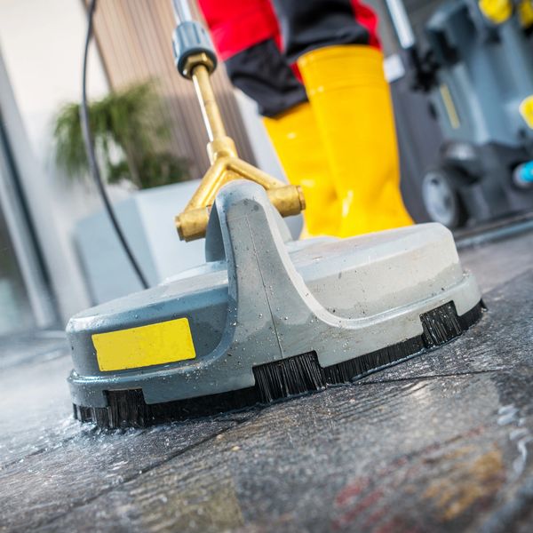 Close-up of a floor cleaning machine with yellow boots in the background.