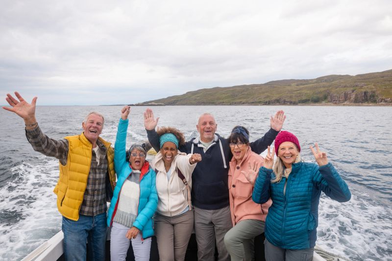 A group of friends enjoying a weekend away together in Torridon, Scotland. They are on a tourboat, enjoying a sightseeing excursion out at sea. They are all standing together and pulling different poses while looking at the camera excitedly.