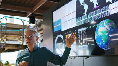 Man presenting global data on a large screen in a modern office.