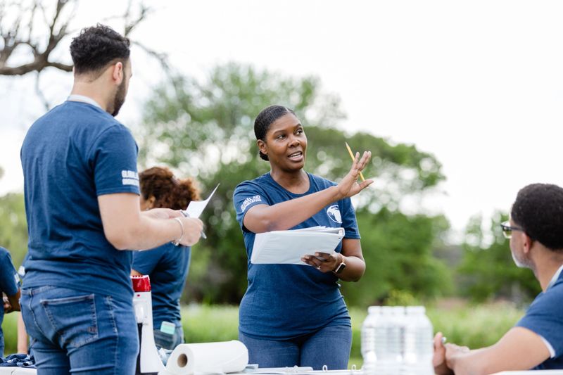 The female team leader gestures to help explain where she would like things set up for the volunteer event at the park.