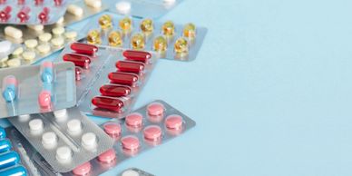 Various colorful pills and capsules in blister packs on a light blue background.