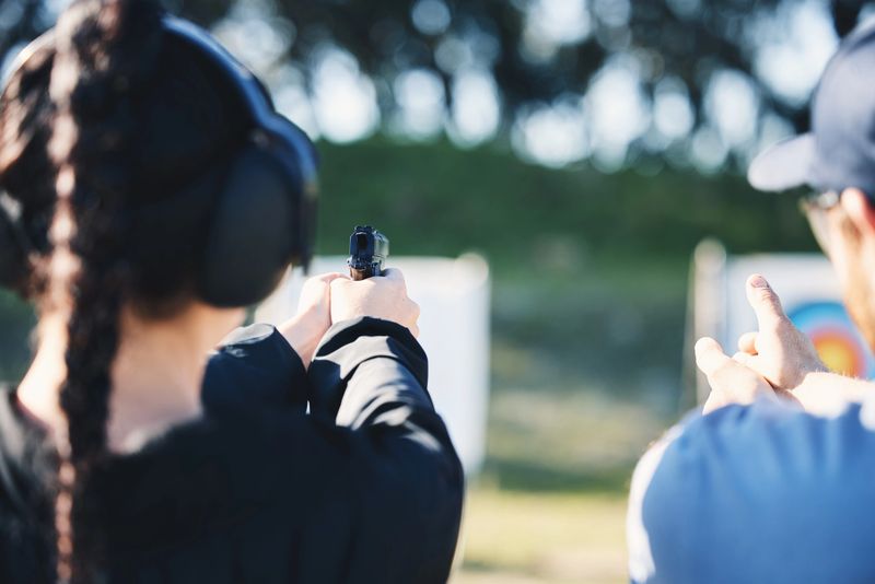 Woman, gun and learning to shoot with instructor at shooting range outdoor for target training. Safety and security with hands teaching woman sport, game or aim with gear and sign for fire or action