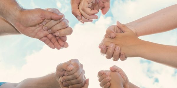Multiple people holding hands in a circle against a blue sky.