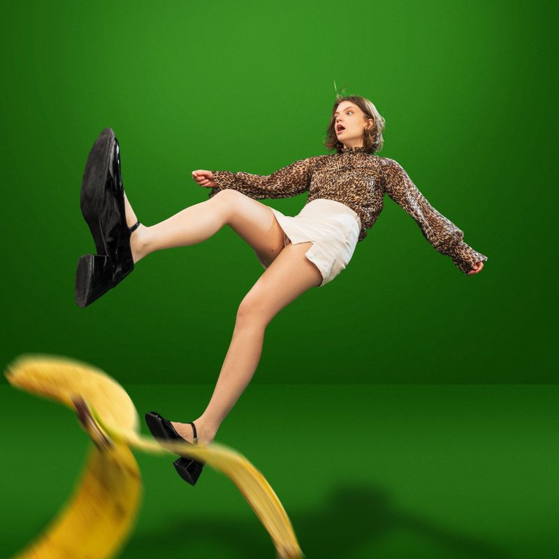 Creative image with young girl in stylish, animal print blouse and white shorts slipping on banana peel and falling down. Concept of emotions, lifestyle, fun, shopping, fashion, ad