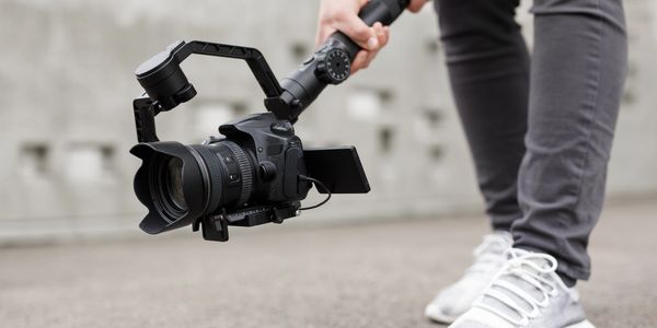 Person holding a DSLR camera mounted on a handheld stabilizer outdoors.