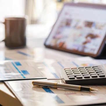 Workspace with calculator, pens, documents, and tablet.