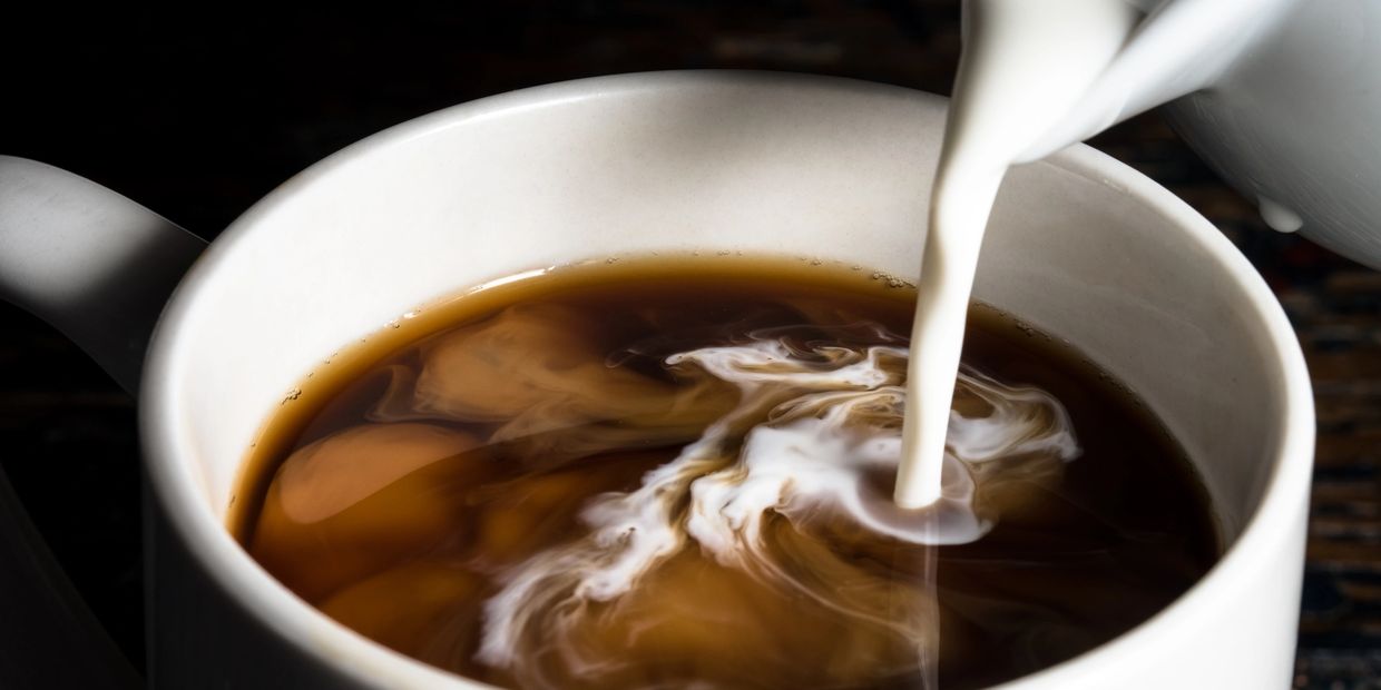 Cream being poured into a cup of coffee, creating swirling patterns.
