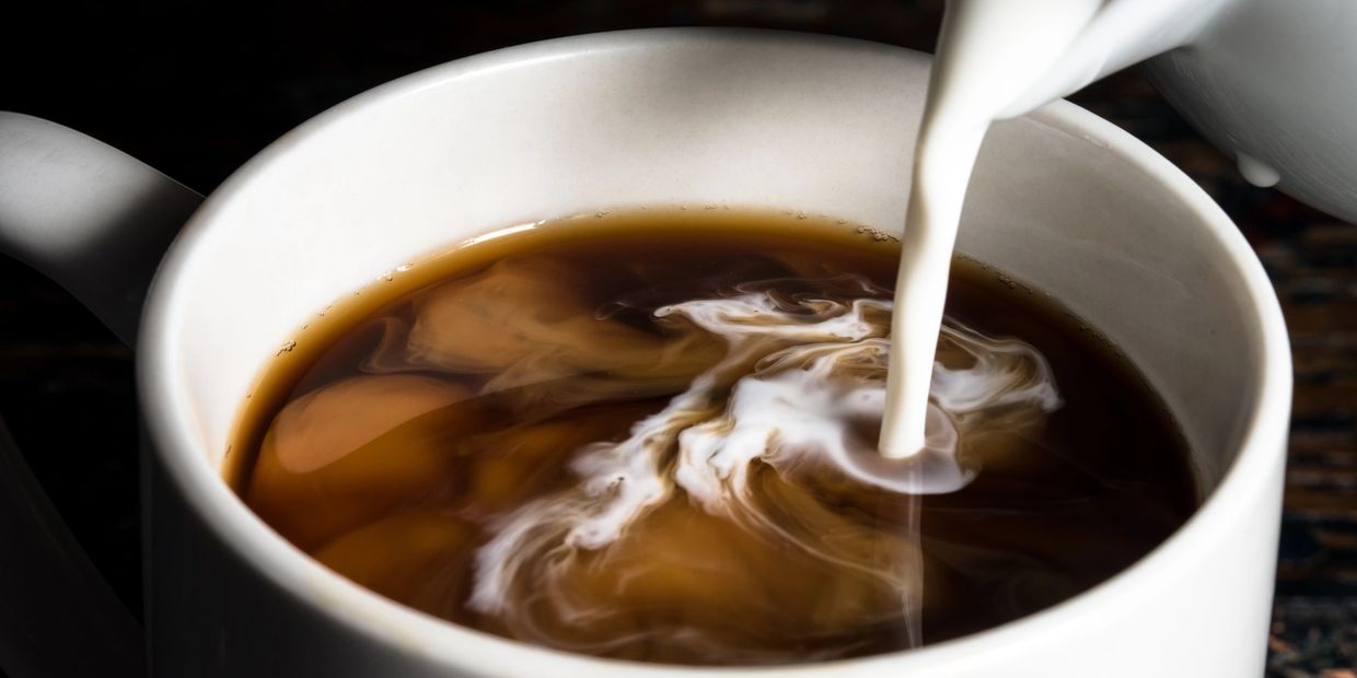 Cream being poured into a cup of coffee, creating swirling patterns.
