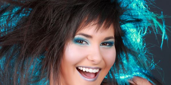 Smiling woman with blue eye makeup and wild hair.