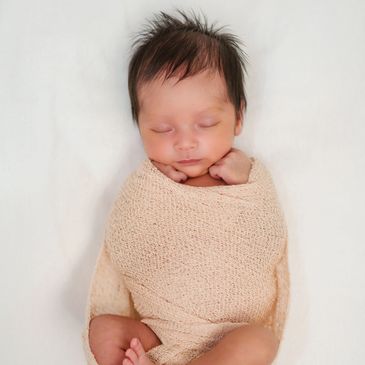 Newborn baby peacefully sleeping, wrapped in a soft beige blanket.
