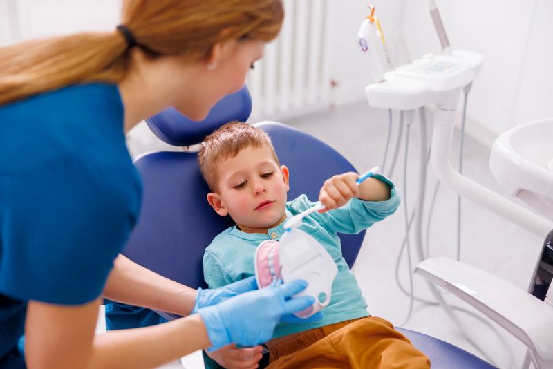 Female dentist demonstrating proper teeth brushing technique to a little boy using tooth brush and plastic human jaw model