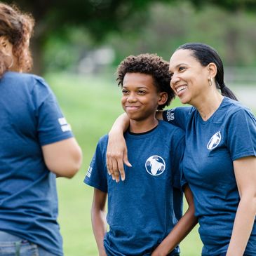 Woman and boy smiling outdoors in matching blue shirts.