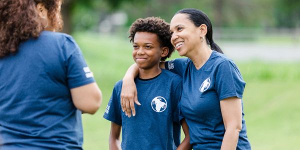 Woman and boy smiling outdoors in matching blue shirts.
