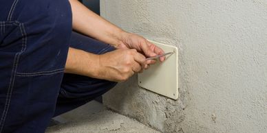 Person fixing or removing a wall plate with a screwdriver.