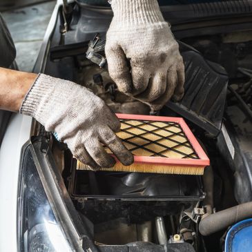 Mechanic replacing a car's air filter with gloved hands under the hood.