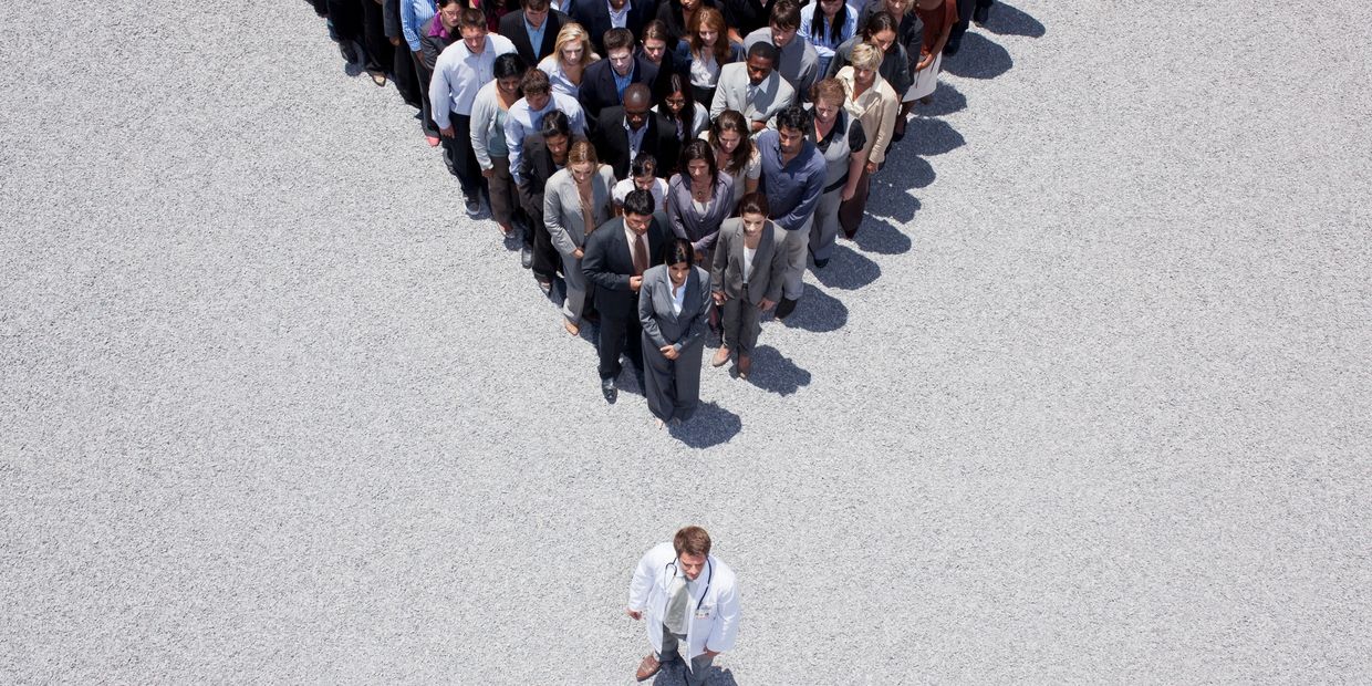A doctor stands apart from a large group of people forming a heart shape.