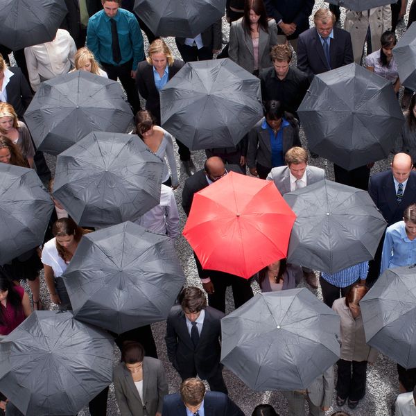 A crowd with one red umbrella among many black ones.
