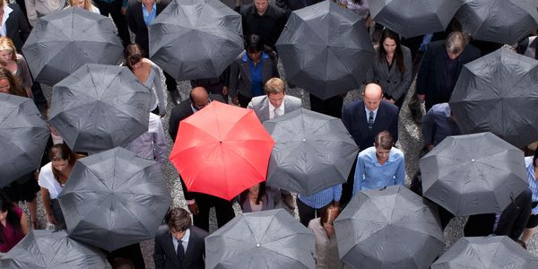 a group of people holding black umbrellas and one in the crowd is holding a red umbrella.