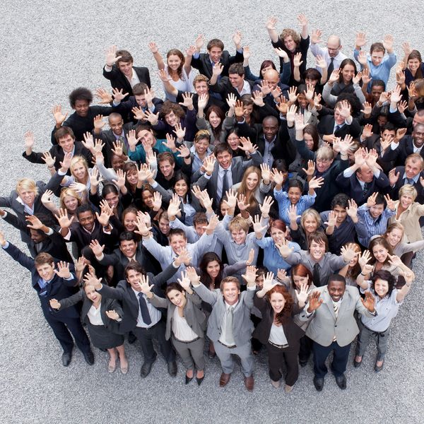 Large diverse group of businesspeople waving and smiling upwards outdoors.