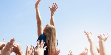 A woman is raised above a crowd under a clear blue sky.