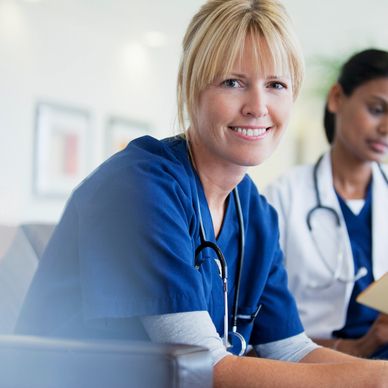 Smiling female nurse in blue scrubs with stethoscope.