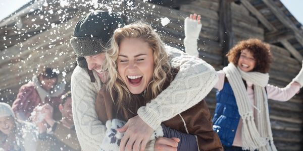 Friends joyfully playing in the snow near a wooden cabin.