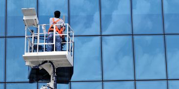 Worker cleaning windows from a lift on a glass building.