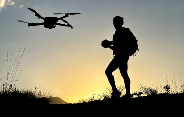 Silhouette of a person controlling a drone at sunset on a hill.