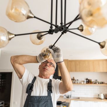A man installs or fixes a modern chandelier in a kitchen.