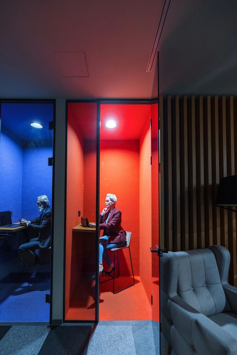 Side view of two mature caucasian male and female employees working in office cubicles. They are sitting, using wireless  technology and wearing causal businesswear.