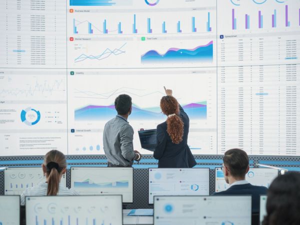 Two professionals analyze financial charts on a large screen in an office.