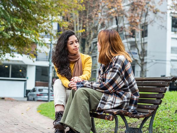 Two women having a serious conversation on a park bench in autumn.