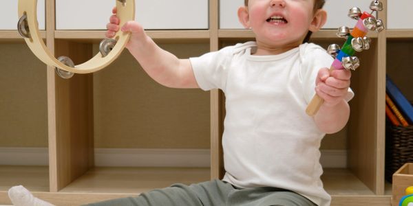A happy toddler playing with a tambourine and jingle bells indoors.
