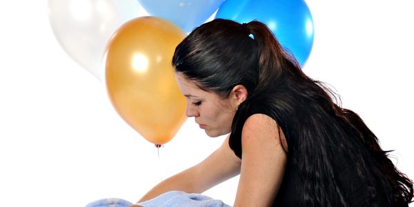 A woman with long dark hair leans over a blue blanket with colorful balloons in the background.