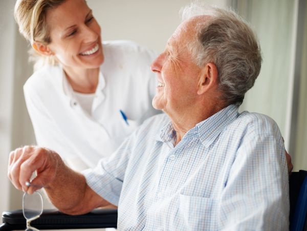 A nurse smiling warmly at an elderly man in a wheelchair.