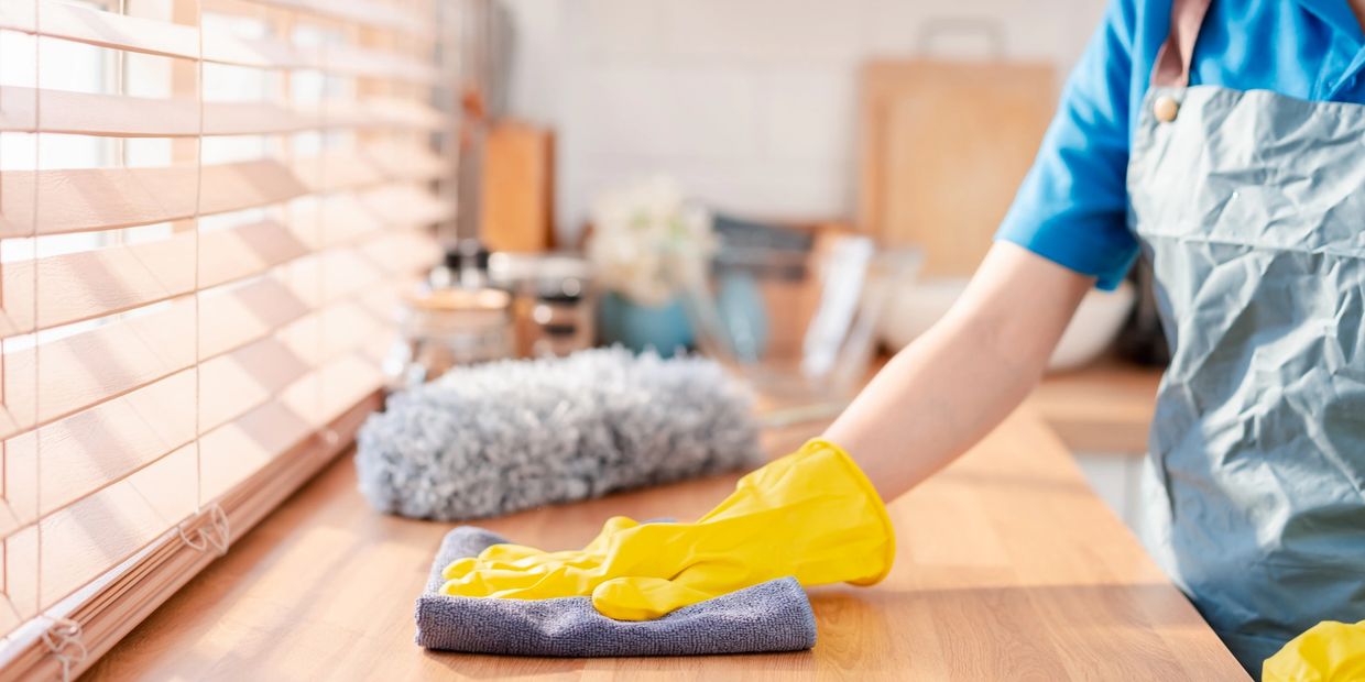 Person cleaning wooden surface with cloth and gloves.