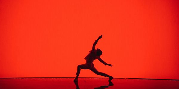 Silhouette of a dancer striking a dynamic pose against a bright red background.