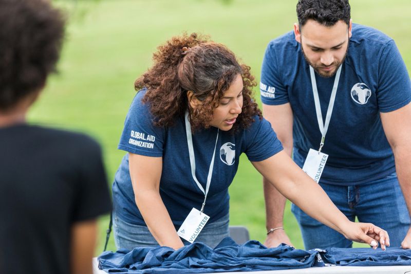 A mature adult female volunteer and her young adult male assistant sort the t-shirts for the event.