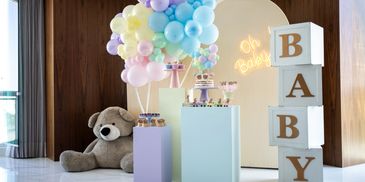 Colorful baby shower setup with balloons, teddy bear, and cake stands.