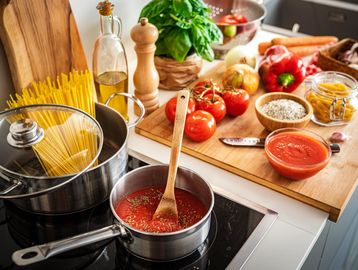 Pot with sauce cooking and fresh ingredients on kitchen counter.