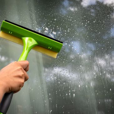 A hand cleaning a soapy window with a green squeegee.