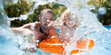 Father and child playing in pool with splash and float.