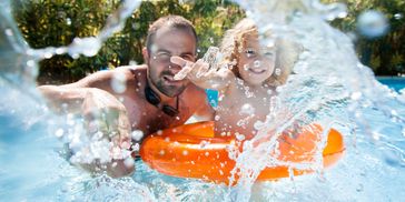 Father and child playing in pool with splash and float.