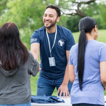Smiling man in blue shirt shaking hands outdoors at an event.