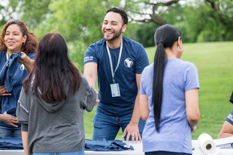 The young adult male smile and shakes hands with the female volunteer who is arriving to help at the park.