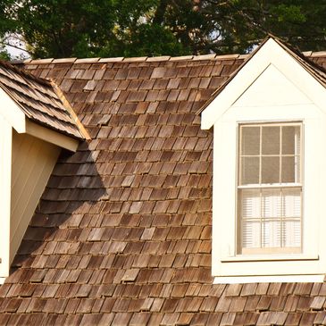 Two dormer windows on a wooden shingle roof.